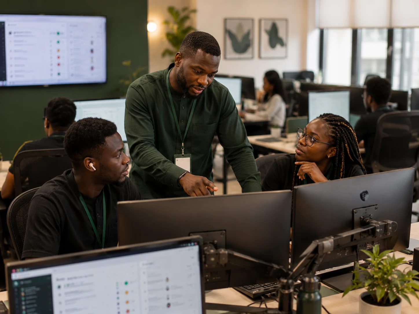 A Gronari team leader beside two colleagues at their desks, talking through the work on their screens.